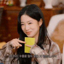 a girl in a plaid shirt is holding a yellow piece of paper and pointing at it