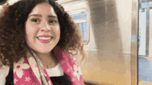 a woman with curly hair wearing a pink louis vuitton scarf smiles for the camera