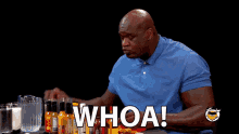 a man in a blue shirt is sitting at a table with bottles of hot sauce and the words whoa above him