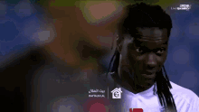 a man with dreadlocks is wearing a white jersey with a soccer ball on the front