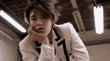 a young man in a white suit is standing in a dark room with his hand on his chin .