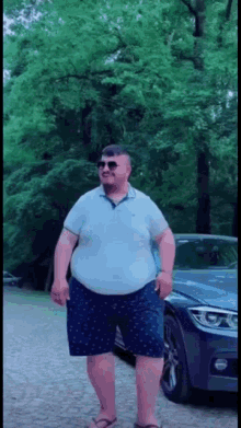 a man is standing in front of a car wearing sunglasses and flip flops .