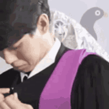 a man wearing a black suit and a purple sash is smoking a cigarette in front of a pigeon .