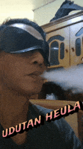 a man wearing a blindfold is smoking a cigarette and the words udutan heula are on the bottom right