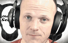 a man wearing headphones looks at the camera in front of an old school sign