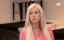 a woman with long blonde hair is wearing a pink sweater and making a funny face .