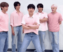 a group of young men standing next to each other wearing pink shirts and jeans