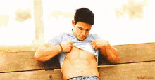 a shirtless man is sitting on a bench looking at his stomach