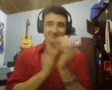 a man wearing headphones and a red shirt is smiling and clapping .