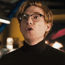 a man wearing glasses and a black turtleneck is making a surprised face