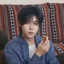 a young man is sitting on a couch eating a sandwich .