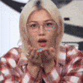 a woman wearing glasses and a plaid shirt is blowing a kiss with her hands .