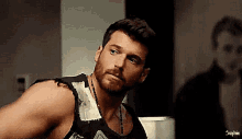 a man with a beard wearing a black tank top is looking at the camera .