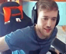 a man is wearing headphones and a blue shirt while sitting in a chair .