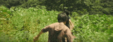 a man and a woman are running through a field of tall grass .