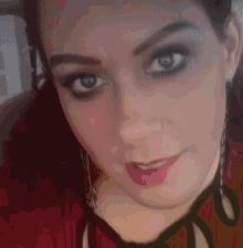 a close up of a woman 's face with a red shirt on and earrings .