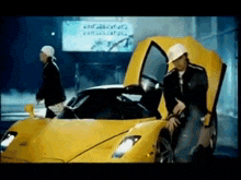 a man is standing next to a yellow sports car with the hood up .
