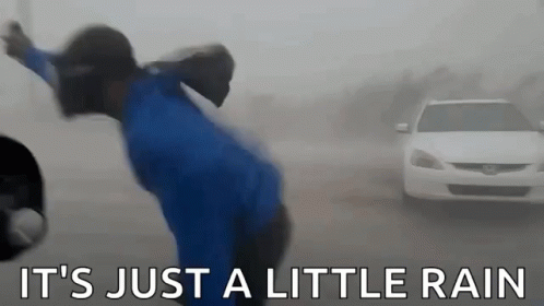 A man stumbling through a torrential downpour with the caption "it's just a little rain"