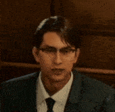 a man wearing glasses and a suit and tie is sitting in a dark room .