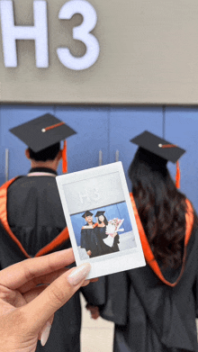 a person holding a picture of two graduates in front of a sign that says " h3 "