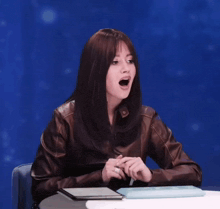 a woman wearing a brown leather jacket is sitting at a table with her mouth open