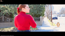 a woman in a red turtleneck is walking down a street