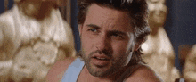 a man with a beard is making a funny face while wearing a tank top .