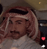 a man wearing a white shirt and a red and white head scarf is sitting in a car