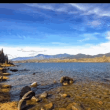 a lake with mountains in the background and rocks on the shore
