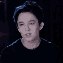 a young man wearing a black shirt is making a funny face in a dark room .