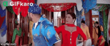 a man in a blue shirt is dancing with a woman in a red dress in a room .
