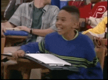 a boy in a blue sweater is sitting at a desk in a classroom