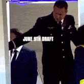 a man in a suit and tie is standing in front of a door that says june 9th draft