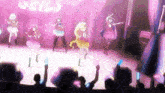 a group of anime girls are dancing on a stage in front of a crowd at a concert .