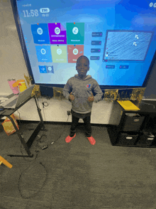 a young boy stands in front of a large screen that says 11:58