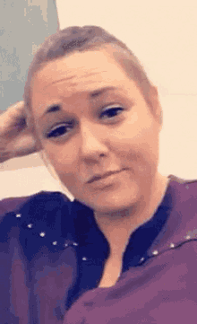 a woman in a purple shirt is making a funny face with her hand in her hair .