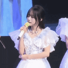 a woman in a white dress holds a microphone in her mouth