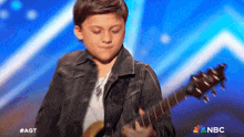 a young boy is playing a guitar on a stage with a nbc logo in the background