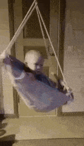 a baby is sitting in a swing hanging from a door .