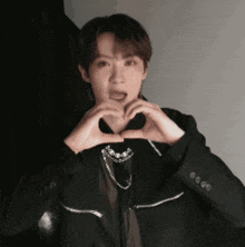 a man in a black jacket is making a heart with his hands