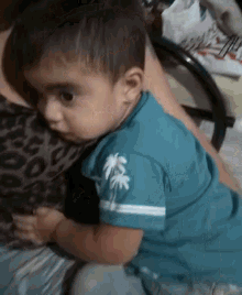 a baby wearing a blue shirt with palm trees on it is laying on a bed .