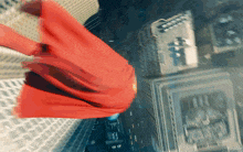 a man in a red cape is flying through the air over a city