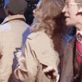 a man in a trench coat and tie is talking to another man in a suit and tie .