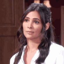 a woman with dark hair and a white shirt is looking at the camera
