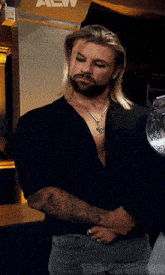 a man with long blonde hair and a beard is standing in front of a wall with the letters aew on it