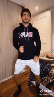 a man in a black hoodie and white shorts is dancing in a room .