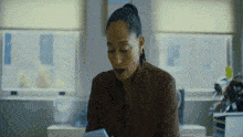 a woman in a brown shirt is sitting in front of a window looking at a tablet .