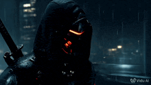 a man in a black hoodie with a red light on his face is holding a sword in the rain