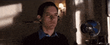 a man in a black sweater is standing in front of a blue fan in a dark room .