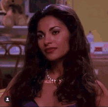 a woman with long dark hair and a necklace is sitting at a desk .